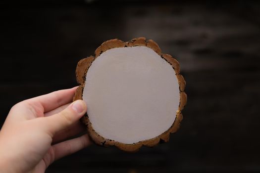 Woman hand holding empty circular piece of wood section texture on dark background. Copy space for text.