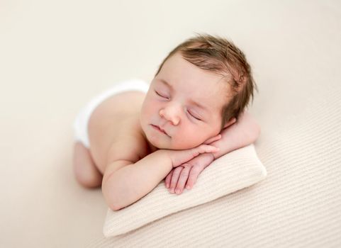 Closeup portrait of adorable newborn baby girl lying on her tummy and sleeping on tiny pillow in studio. Cute infant child napping holding hands under cheeks