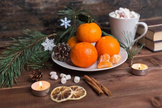 Christmas still life with fresh mandarines, marshmallows in a cup, lighted candles and cinnamon on wooden background. Nature New Year concept in instagram style