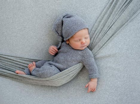 Newborn baby boy wearing in knitted costume sleeping in hammock. Infant kid studio portrait with decoration