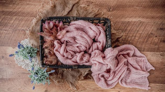 Cute cozy background for newborn photosession with flowers hydrangea. Digital composite with basket filled with soft color pink knitted blanket and standing on sackcloth