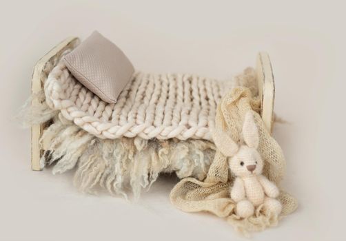 Wooden stylized small furniture bed with pillow and knitted blanket for newborn photoshoot in beige colors. Designed decoration object for infant studio photo