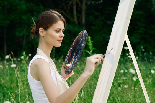 Woman in white dress with palette of paints on nature art drawing. High quality photo