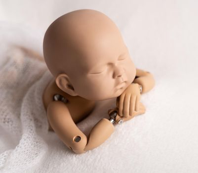 Realistic plastic figure of newborn child for photographing practice, with head on hands, isolated on white background