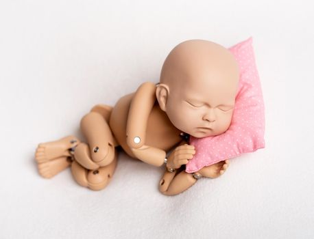 Accurate doll of newborn baby on pink pillow for photo practicing, on white background