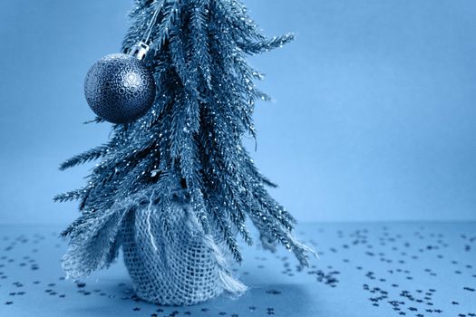 Christmas tree with toy is on blue table with stars on the table and blue background behind the tree. New year and christmas concept, everything is toned in classic blue, Copyspace for the text,