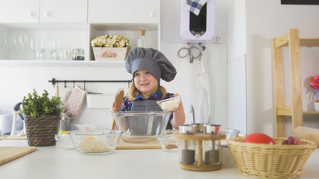 Little girl baker puts batter to the pastry dough for cooking biscuits, close up