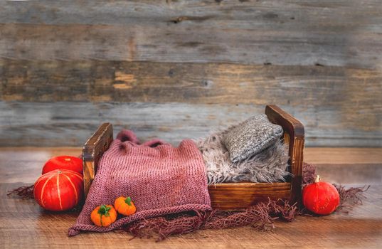 Tiny wooden bed for newborn baby photoshoot decorated with autumn pampkins, knitted blanket and toys. Studio handmade scene for halloween infant child photos
