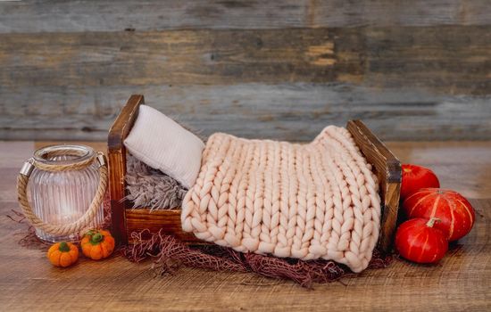 Stylized wooden bed for newborn baby photoshoot decorated with autumn pampkins, knitted blanket and toys. Studio handmade scene for halloween infant child kid photos