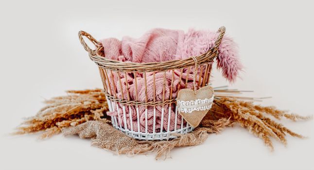 Tiny basket decor for newborn studio photoshoot filled with knitted blanket and toy heart closeup. Infant baby handmade furniture
