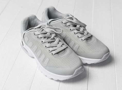 Gray cozy running shoes sitting on white wood, long shoelaces tied in, white soles