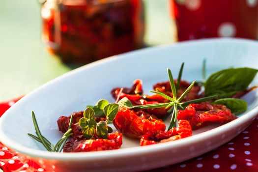 sun dried tomatoes on a white plate with fresh herbs - rosemary, basil and oregano