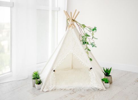 Beautiful white hut decoration for newborn photosession with plants and fur in light room. Stylish furniture wigwam for infant child studio photo