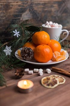 Christmas still life with fresh mandarines, marshmallows in a cup, lighted candles and cinnamon on wooden background. Nature New Year concept in instagram style