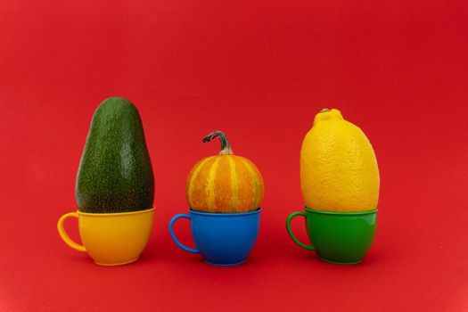 Avocado, pumpkin, lemon in colorful small mugs on red background. Enough space for text.