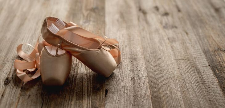 Pink pointe shoes with ribbons on wooden background, top view