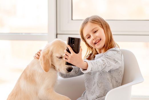 Cheerful little girl making selfie with her dog at home