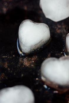 Ice in form of hearts on black background starting to melt
