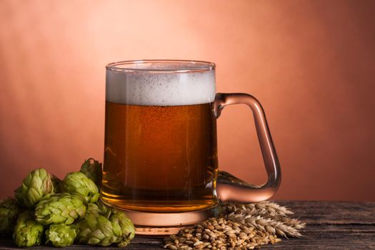 Glass of beer with hops and barley on the wooden table