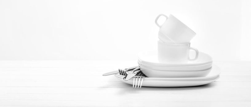 Empty white plates, cups and silver cutlery on light white background. Close-up