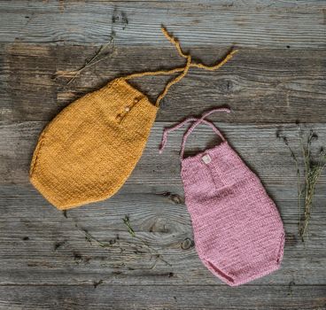 two colorful yellow and pik knitted overalls for newborn baby on wooden background, top view