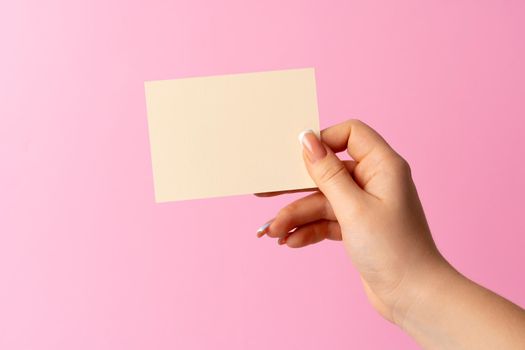 Woman hand showing blank business card on pink background. Close up.