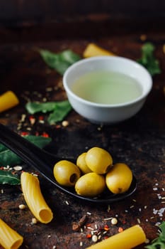 Olives in black spoon surrounded by other ingredients.