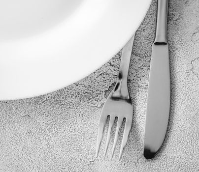 Stainless fork and knife with white plate, top view with copy space