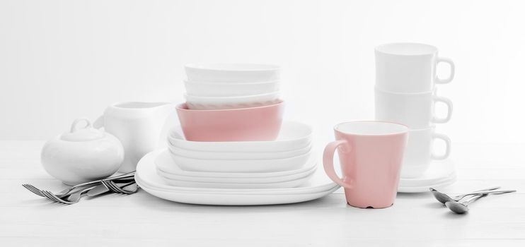 White and pink plates, sugar bowl and mugs on light background. Ceramic tableware.