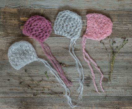 set of tender knitted pink and white hats for newborn on wooden background