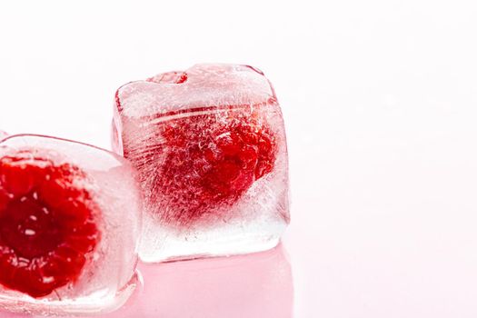 Raspberry ice cubes on pink glossy background. Close up.
