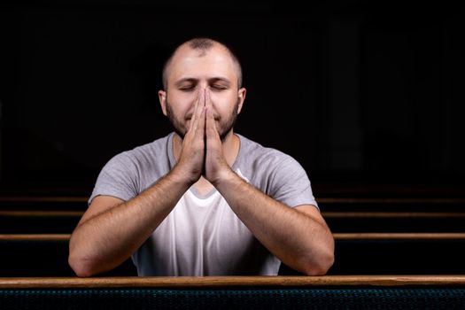 A Christian man in white shirt is sitting and praying with humble heart in the church.