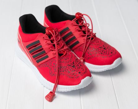 Bright red running shoes with black stripes on side, long shoelaces on white background