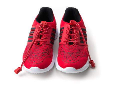 Bright red running shoes with black stripes on side, long shoelaces isolated on white background