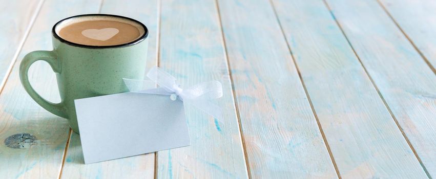 Cup of cappuccino with lovely gift card label with bow on blue rustic background. Happy Valentine's Day, Happy Birthday, Women's day, Mother's day. Greeting card message, copyspace