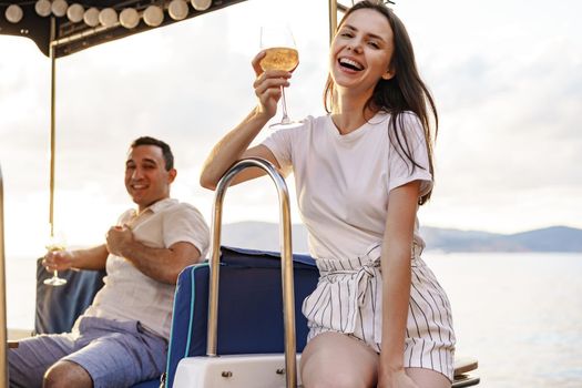 Young loving couple sitting on the yacht deck and drinking wine together