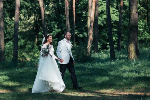 Bride and groom are walking in the woods on their wedding day.