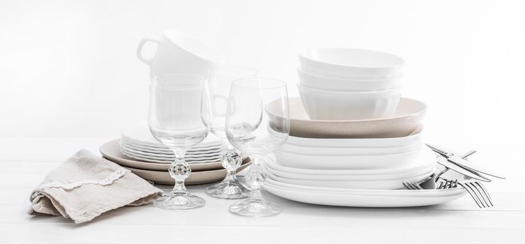 Stack of mixed white and beige dishes and crystal glasses on white background