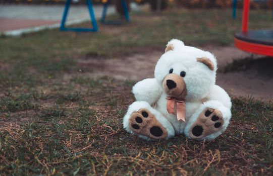 Cute adorable lost abandoned soft plush stuffed children toy teddy bear sitting on ground street road. In park outdoor. Lost lonely toy outside.