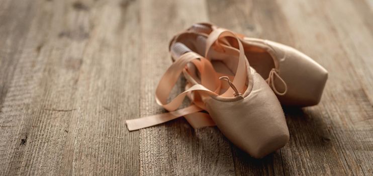 Pink pointe shoes with ribbons on wooden background, top view