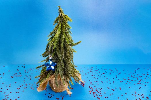 Green tree with small blue toy is on blue table with red stars on the table and there is blue background behind the tree. New year and christmas concept. Copyspace for the text, good for banner.