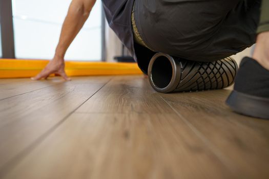 Close up of a man massaging his muscles by the foam roller in gym