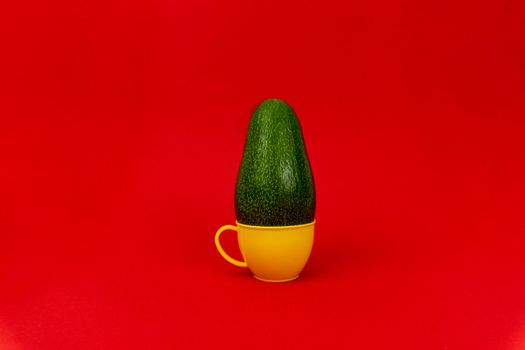 Green avocado in a plastic yellow mug in red background, minimalistic concept, enough space for text.