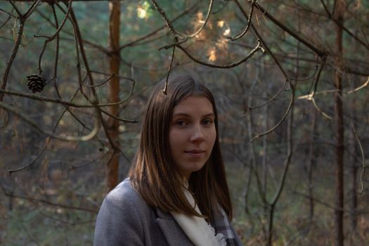 Half-turned girl in a gray coat, which stands in the forest on a sunny autumn day