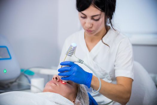 Cosmetology clinic. A client taking procedure. A woman cosmetologist working with a tool. Close up