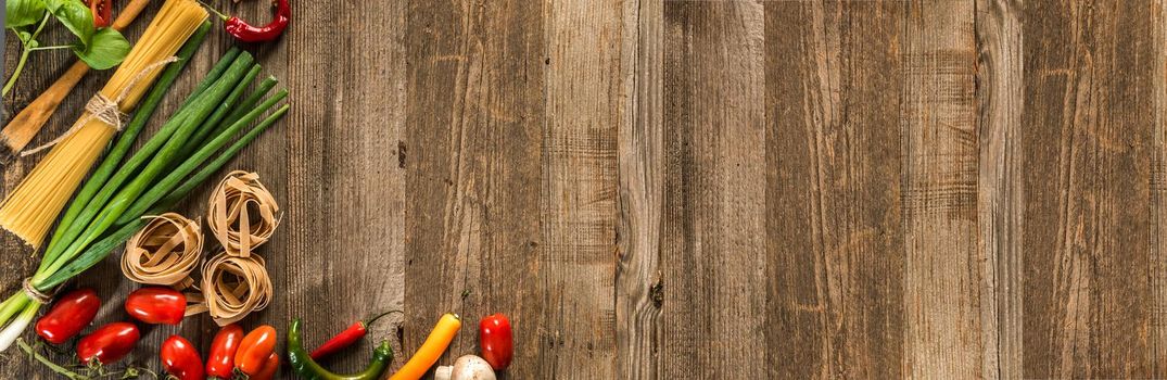 Italian food background with raw pasta and vegetables on wooden table