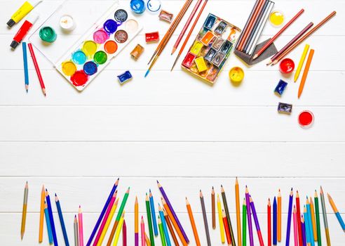 Row of multicolored pencils and watercolors with brushes on white wooden background, copyspace, top view. Still life of various drawing tools