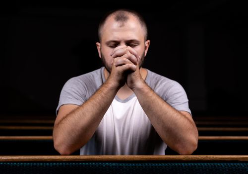 A Christian man in white shirt is sitting and praying with humble heart in the church.