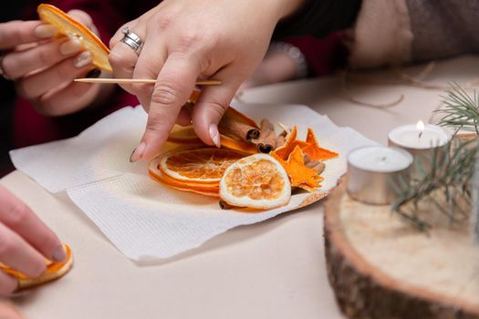 Women's hand making decorations from dried oranges, stars from tangerine and cinnamon. Girls party or meeting.