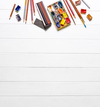 Top view of brushes, gouache and colored pencils on white wooden background. Accessories for drawing. Copyspace, empty space for text
